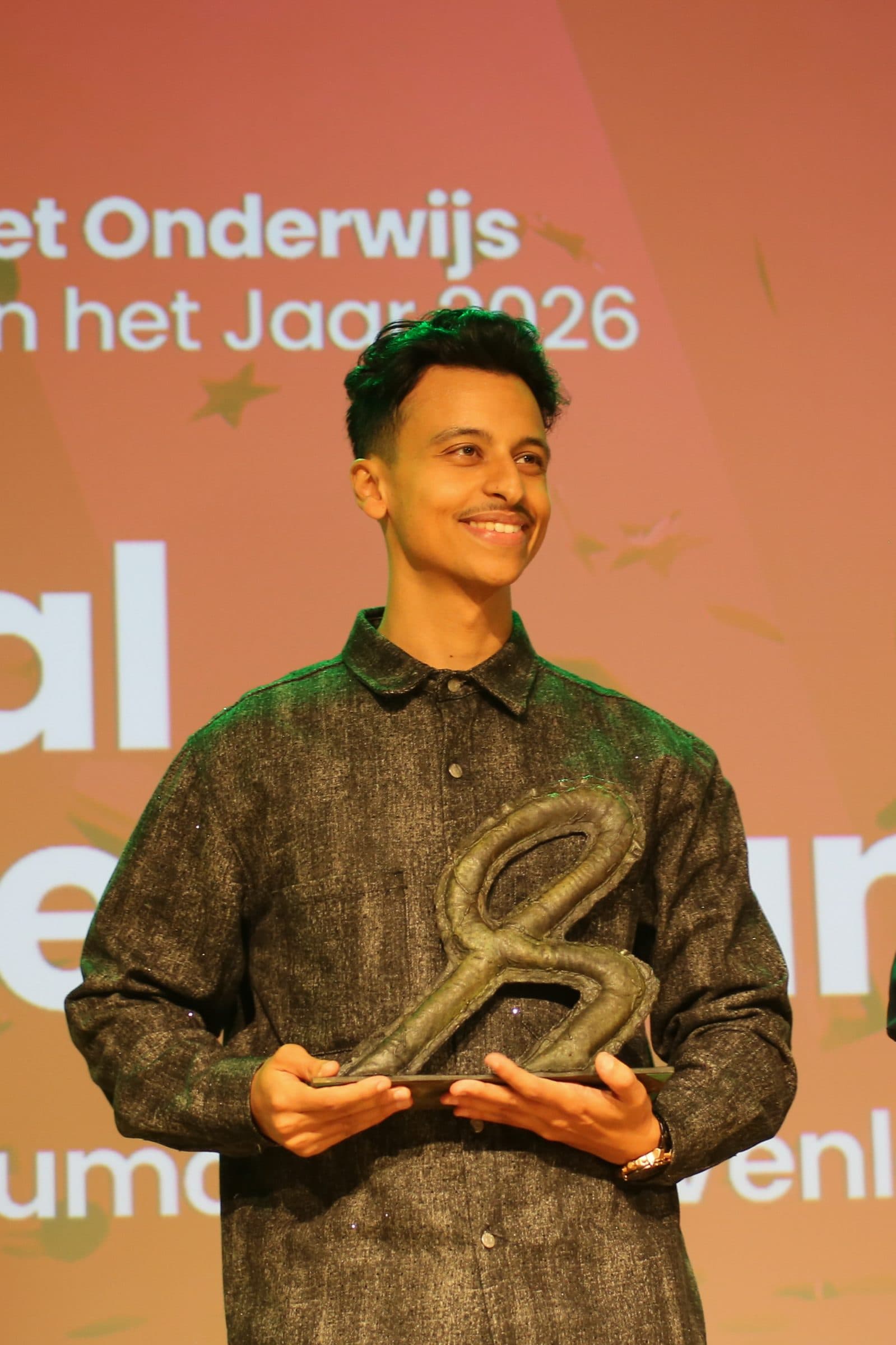 Bilal met de trofee van Leraar van het Jaar 2026 voor het podiumscherm met zijn naam