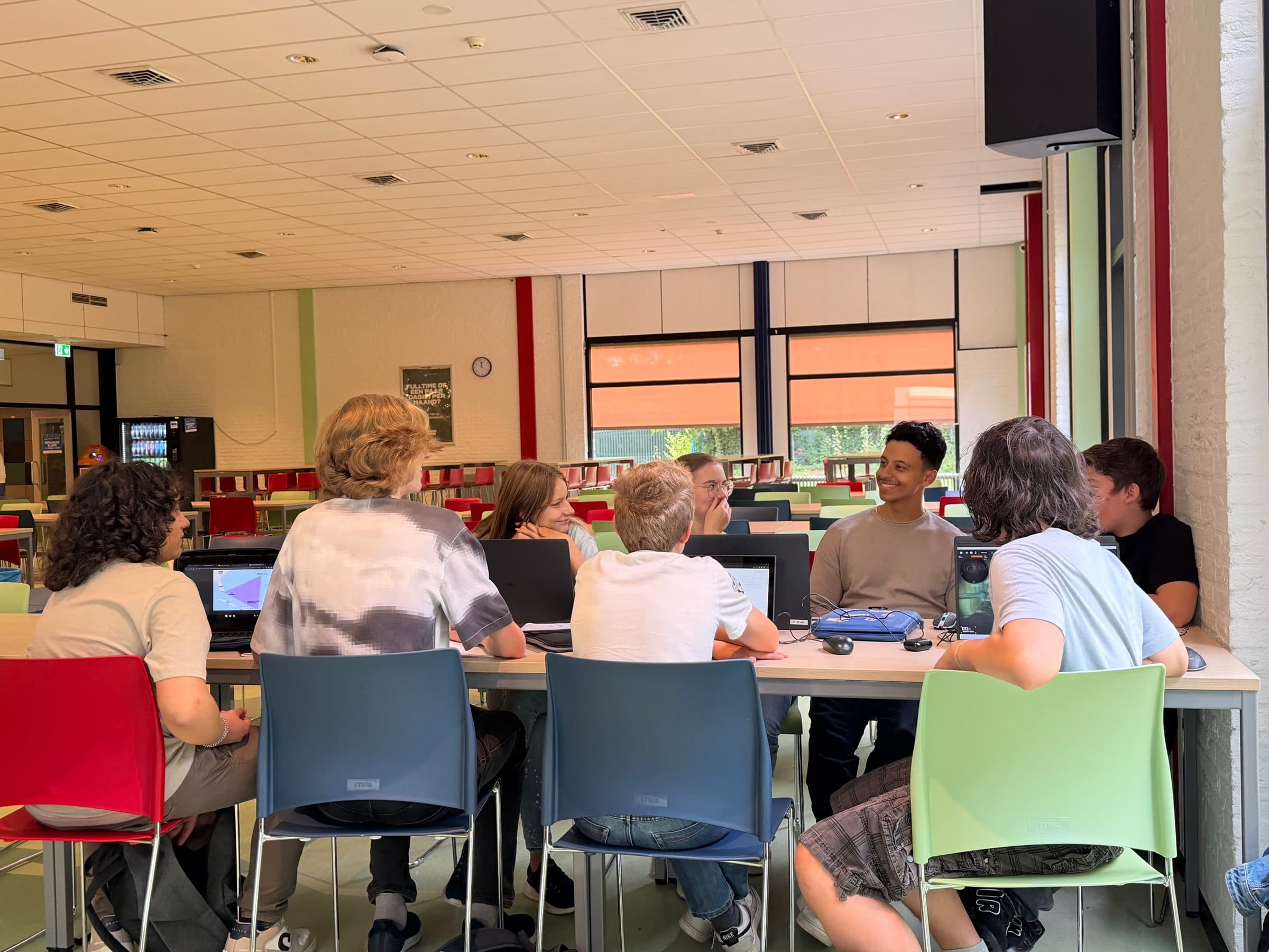 Bilal tussen zijn leerlingen die aan lange tafels op laptops werken